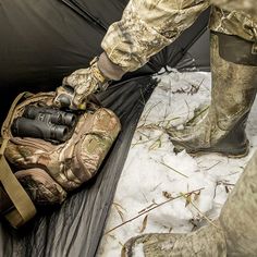 a man standing next to a tent in the snow with his boots and gear on