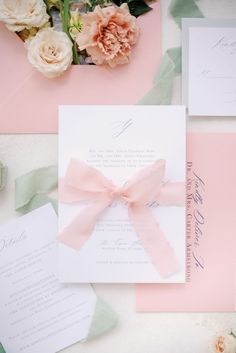 the wedding stationery is laid out on top of pink and white paper with flowers