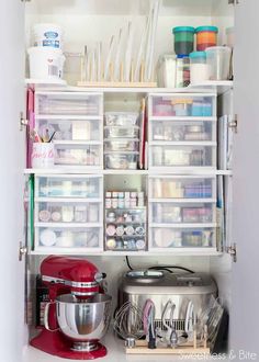 an organized pantry with plastic containers, mixer and other kitchen supplies on shelves above the counter