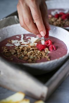 a person picking up some fruit from a bowl with granola on it and another hand reaching for something in the bowl