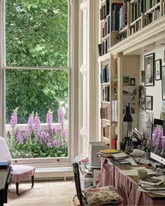 a room with lots of bookshelves and purple flowers in the window sill