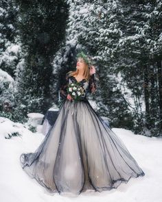 a woman standing in the snow wearing a dress with long sleeves and flowers on her head