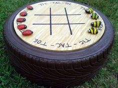 a wooden tic - tac - toe game sitting in the grass with ladybugs on it