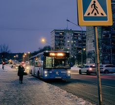 a blue bus driving down a snow covered street next to tall buildings and traffic lights