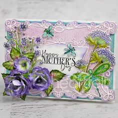 a mother's day card with purple flowers and dragonflys on it, next to a doily