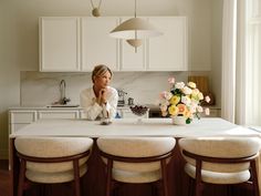 a woman sitting at a kitchen table in front of a vase with flowers on it