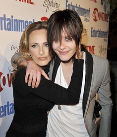 two people standing next to each other in front of a red carpeted wall with the words entertainment on it