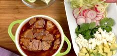 a bowl of meat and vegetables next to a plate of salad on a wooden table