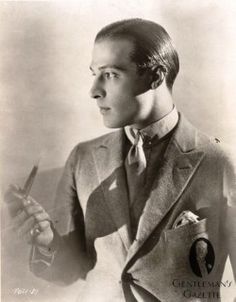 an old black and white photo of a man in a suit holding a pair of scissors