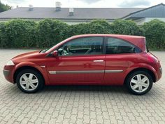 a small red car parked in front of a hedged area with bushes behind it