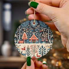 a hand holding a christmas ornament with a house in the woods on it