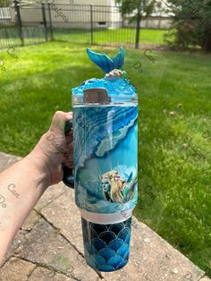 a hand holding a blue and white cup with an image of a mermaid on it