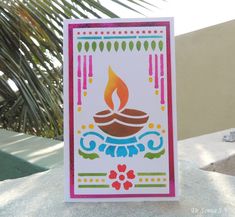 a birthday card with a lit candle in the middle on top of a table next to a palm tree