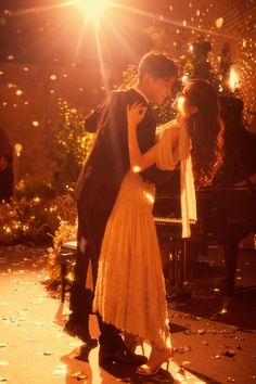 a man and woman dance in front of a piano at night with lights on the ground