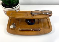 a wooden tray with glasses, pen and money on it next to a potted plant