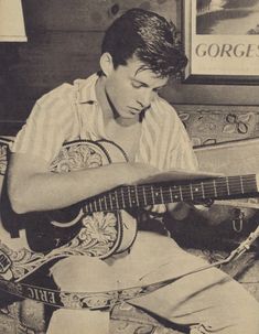 a young man sitting on the floor playing an acoustic guitar with his eyes closed and hands clasped