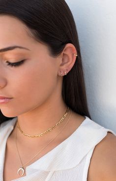 a woman wearing a white top and gold chain necklace with an open circle on it