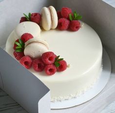 a white cake with raspberries and macaroons on top in a box