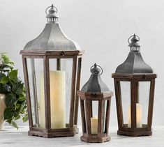 three wooden lanterns with lit candles sitting on top of a table next to a potted plant