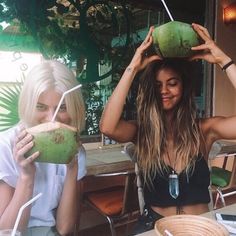 two women sitting at a table with drinks and fruit in front of their faces,