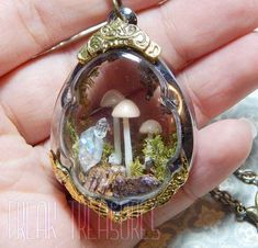 a hand holding a glass pendant with mushrooms and other things in it's center