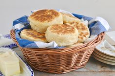 some biscuits are sitting in a wicker basket on a table with plates and butter