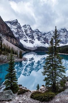 an image of a lake in the mountains with snow on top and trees around it