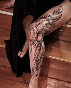 a woman's legs with tattoos on them sitting on the floor next to stairs