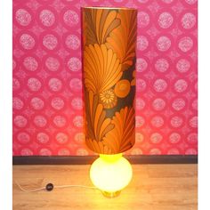 a lamp that is on top of a wooden floor next to a wall with pink and orange designs