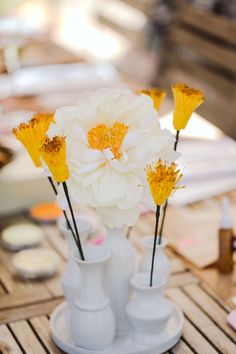 three white vases with yellow flowers in them on a wooden table next to other items