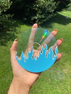 a hand holding a blue disc with flames on it in the middle of a grassy area