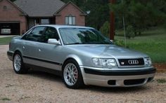 a silver car is parked in front of a brick house on a gravel driveway with grass and trees behind it