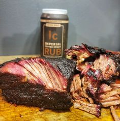 a large piece of meat sitting on top of a wooden cutting board next to a can of beer