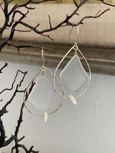 a pair of earrings hanging from a tree branch in front of a window sill