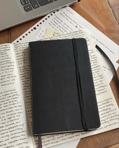 a notebook sitting on top of an open book next to a laptop computer and papers