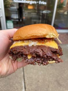 a hand holding a hamburger with cheese and meat