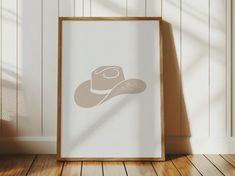 an empty frame with a hat on it in front of a white wall and wooden floor