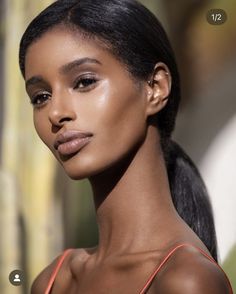 a close up of a woman with dark hair wearing an orange tank top and earrings