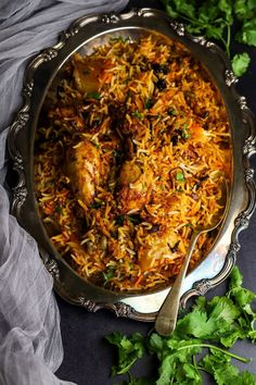 a silver platter filled with rice and chicken next to cilantro leaves on a table