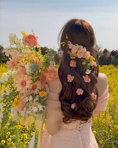 a woman with flowers in her hair walking through a field full of yellow and pink flowers