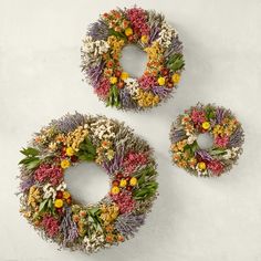 three wreaths with flowers on them sitting next to each other in front of a white wall