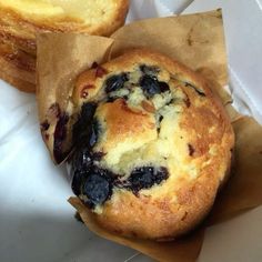 two blueberry muffins sitting on top of brown paper in a white container