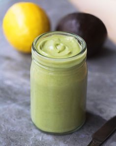 a jar filled with green liquid next to two lemons and an eggplant