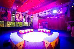 a brightly lit room with purple and red lights on the ceiling, round seating area