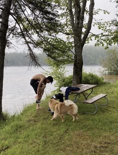 a man is playing with his dog by the water's edge near a picnic table