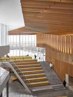 two people are walking up and down the stairs in an open area with large windows