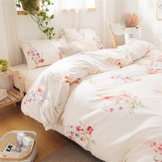 a white bed with pink flowers on the comforter and pillow cases in front of a window