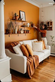 a living room with orange walls and white couches, potted plants on the shelves