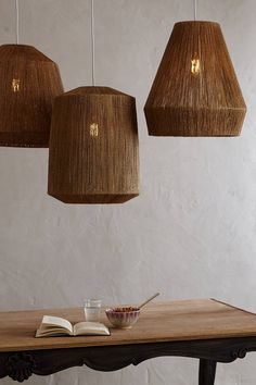 three lamps hanging from the ceiling above a table with a book and bowl on it