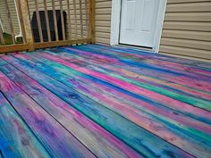 a wooden deck with multicolored paint on it and a white door in the background